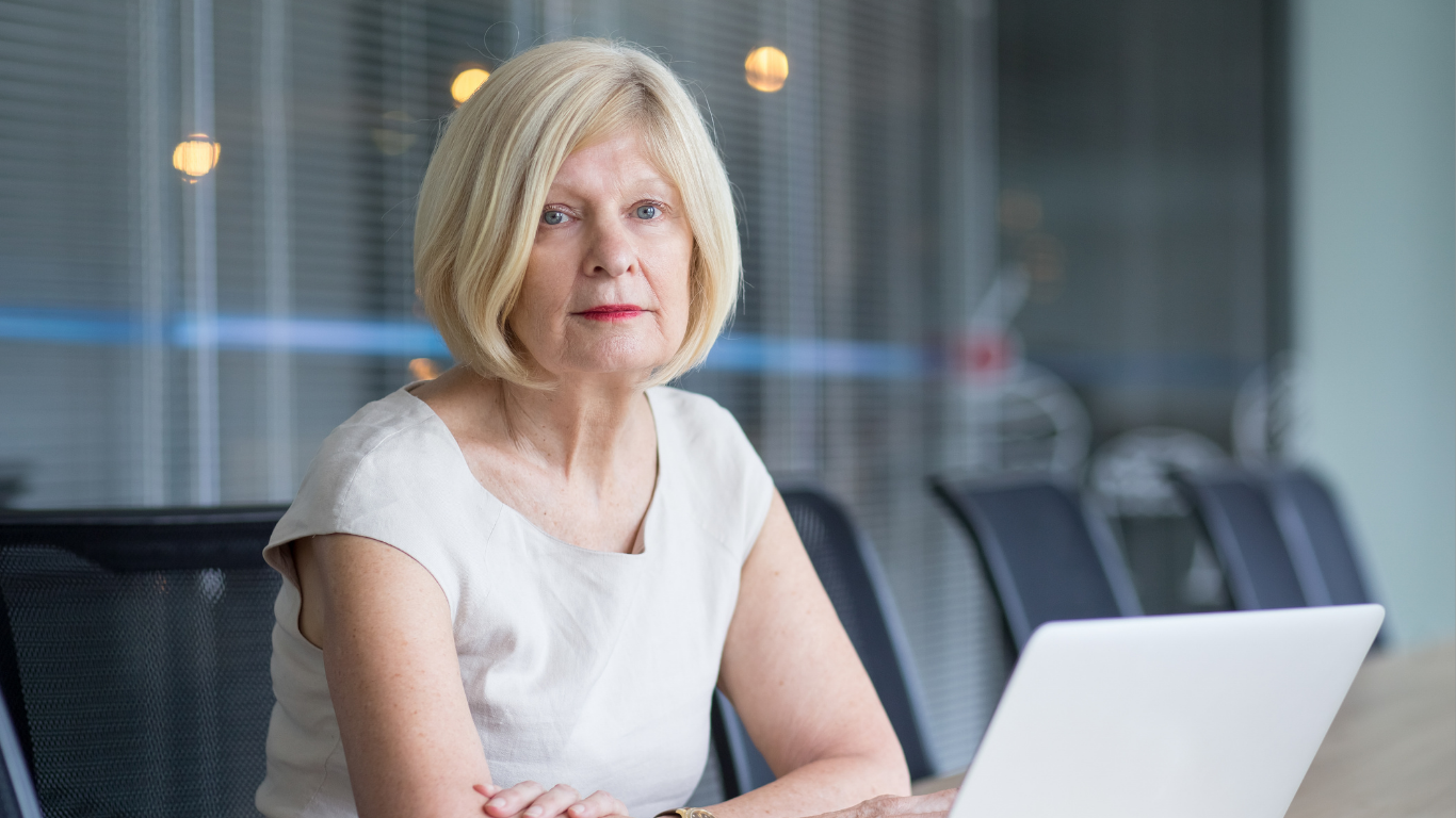 Senior female club board member in boardroom setting with laptop