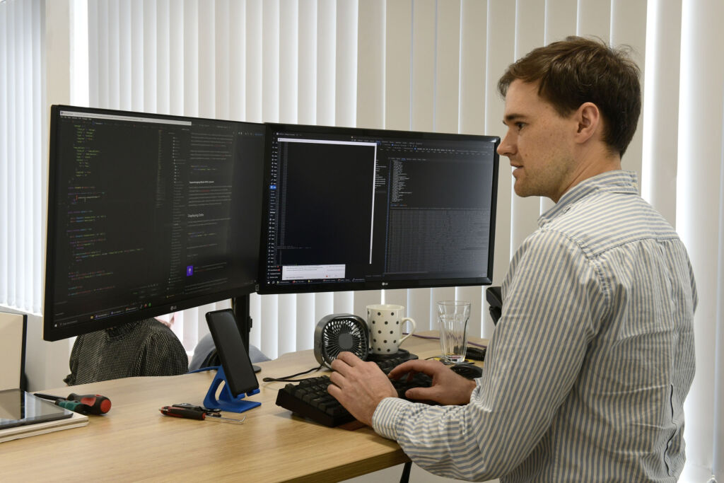 Peter writing code at a dual-monitor desk in the Web Bird Digital office